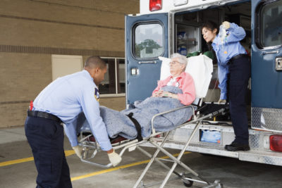 Paramedics putting senior woman into ambulance at a safety net hospital