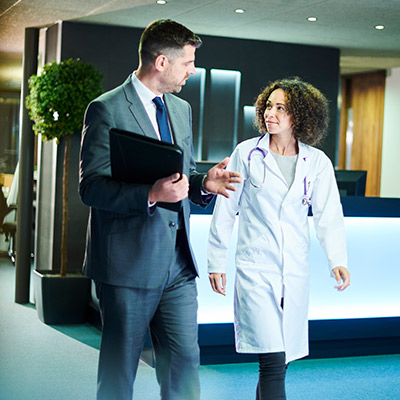 Male business man and female doctor talking about referral coordination while walking together in the office.